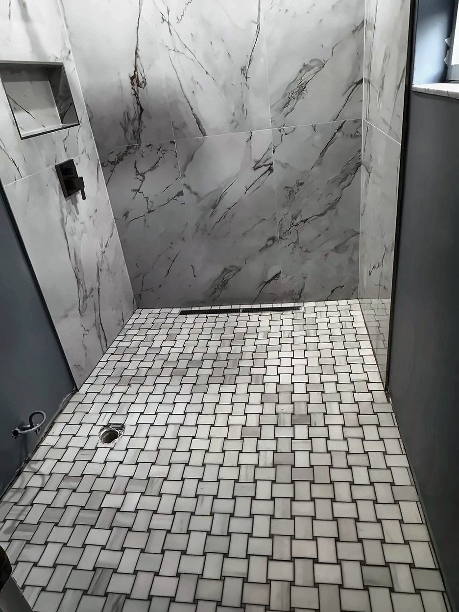 Basketweave mosaic shower floor draining to a linear grate with slab walls and a recessed niche