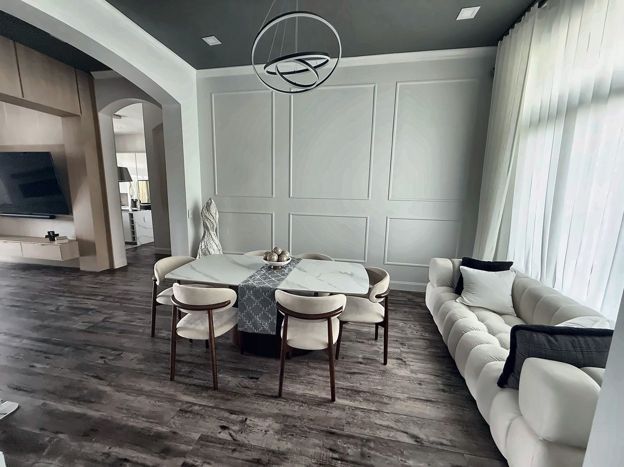 The same dining room after renovation: a full-height applied moulding panel wall, a deep green painted ceiling, floor-to-ceiling sheers on the tall window and a sculptural ring chandelier over a marble table