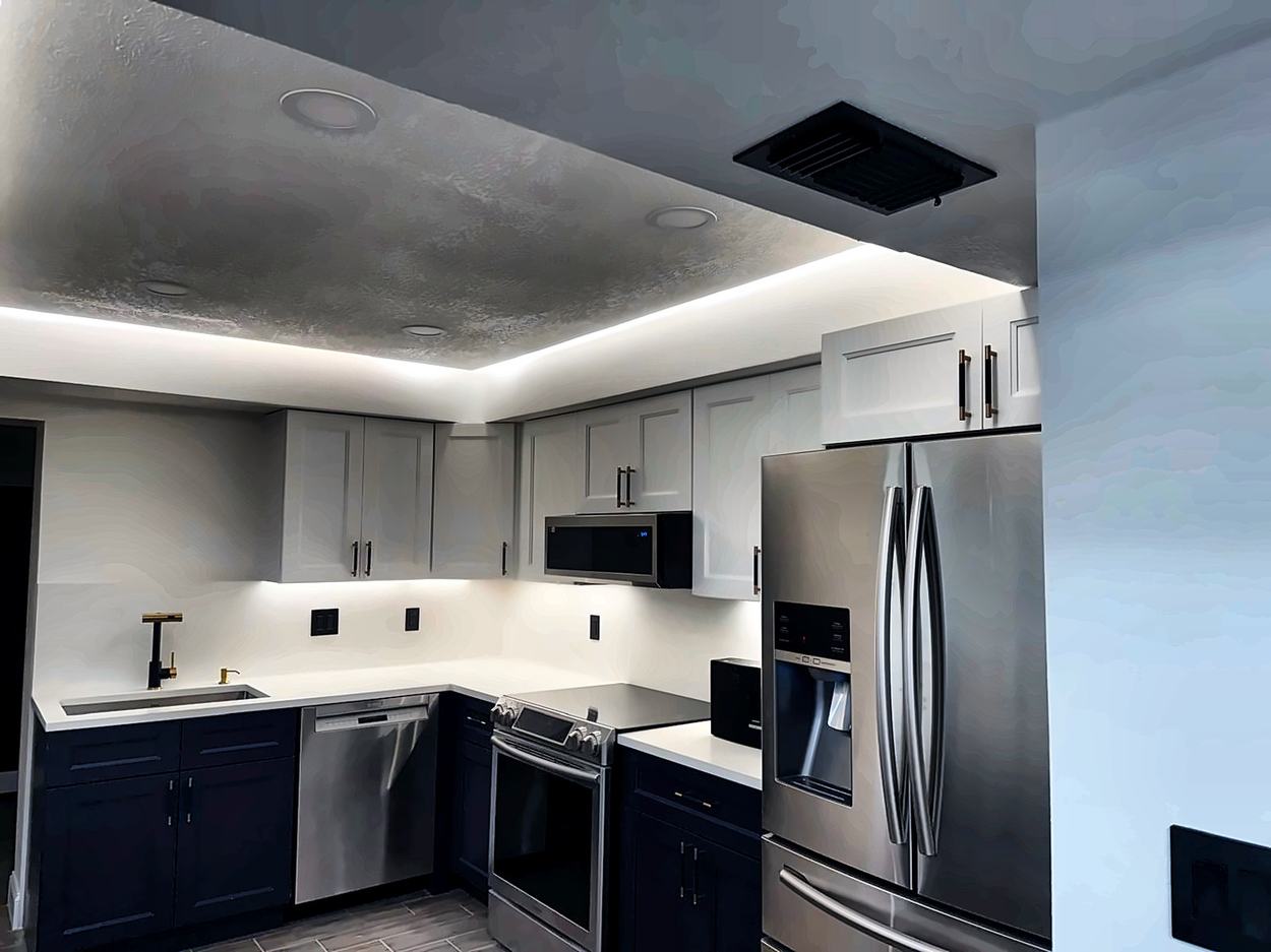 Finished kitchen with navy lower cabinets, white uppers, quartz counters, brass hardware and cove lighting